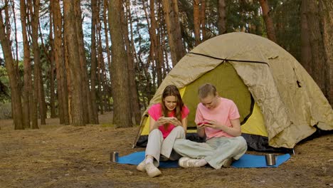 two friends camping and playing on their phones in the woods