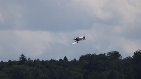 tracking shot of hobby light aircraft with propeller in the air during cloudy day in scenic woodland area