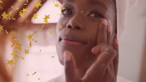 Animation-of-gold-stars-floating-over-happy-african-american-woman-cleansing-face-in-bathroom