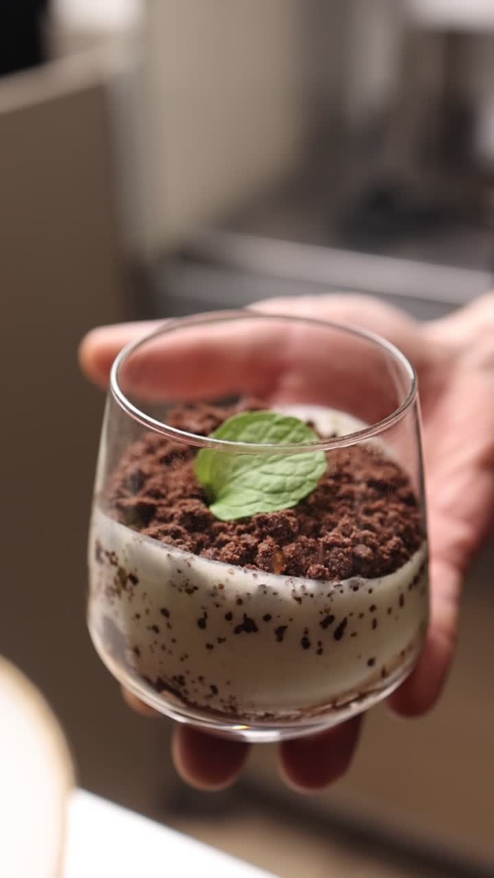 Mano che tiene un delizioso dessert al cioccolato e menta in un bicchiere