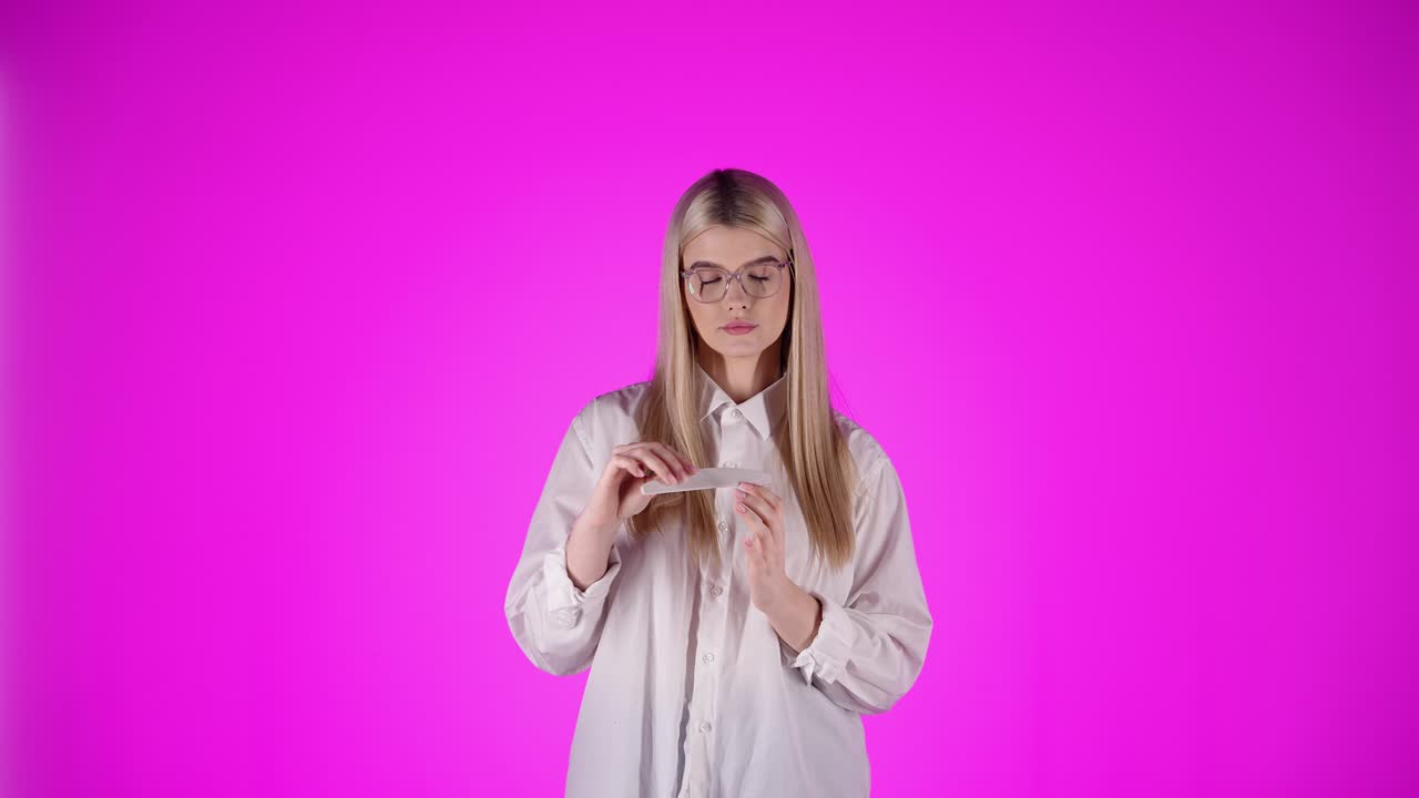 joven rubia aburrida hace manicura, limpieza de uñas, mirando a la cámara