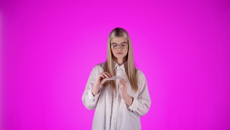 bored young blonde woman does manicure, filing fingernails, looking at camera
