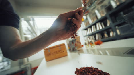 Primer-Plano-De-La-Mano-De-Un-Hombre-Recogiendo-Brillantes-Hierbas-Aromáticas-Secas-De-Una-Mesa