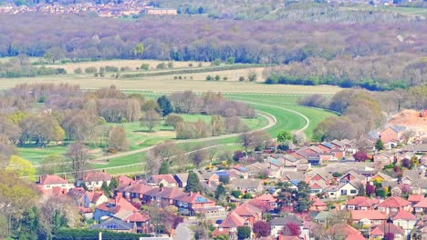 drone captures a horse racing track in doncaster with a green curving racecourse surrounded by suburban houses and tree-lined fields, showcasing a peaceful countryside environment
