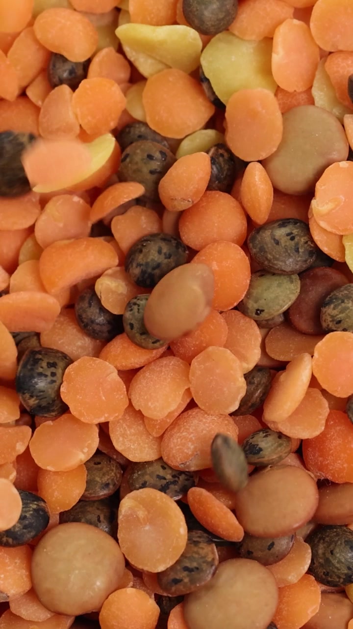 A vibrant mix of orange, yellow, and brown lentils falling in a vertical frame.