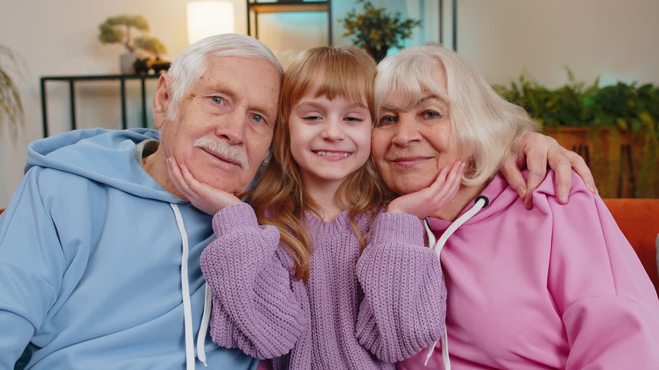 Portrait of smiling kid granddaughter and loving grandfather and grandmother looking at camera home