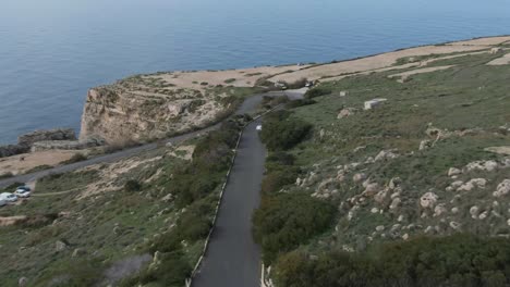 car driving on the curved road uphill overlooking the blue sea - aerial shot