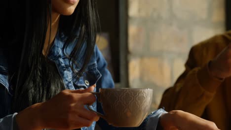 Close-up-of-young-beautiful-mixed-race-woman-drinking-coffee-and-using-mobile-phone-in-cafe-4k