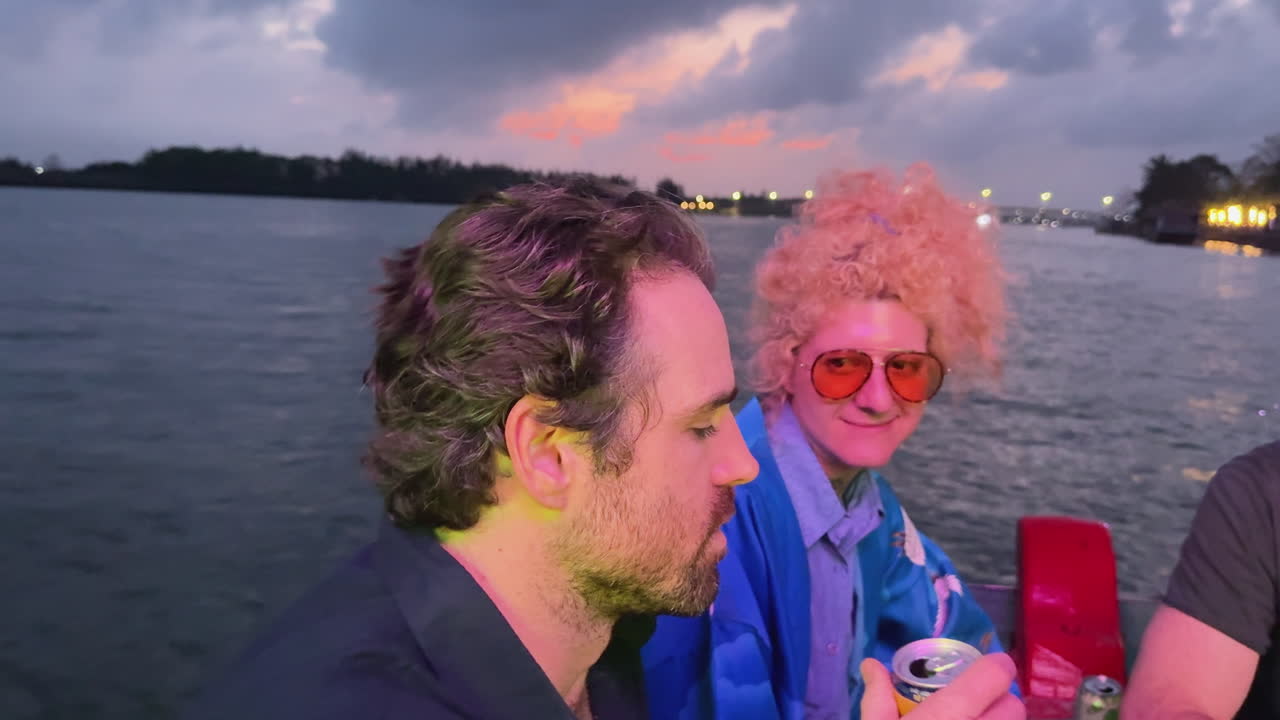 Amici che si godono un giro in barca al tramonto sul fiume Hoài di Hoi An, con luci serali colorate, bevande e un'atmosfera rilassata da crociera-festival in Vietnam