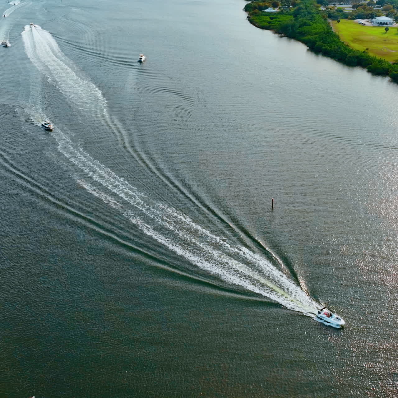 Few motor boats are on the water. Drone footage descending above the river on sunny day.