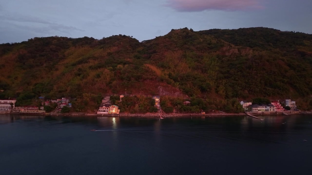 Riprese aeree con drone di una barca da pesca solitaria che naviga su acque tropicali calme al tramonto di fronte alla costa di Anilao, creando un paesaggio marino pacifico e suggestivo.