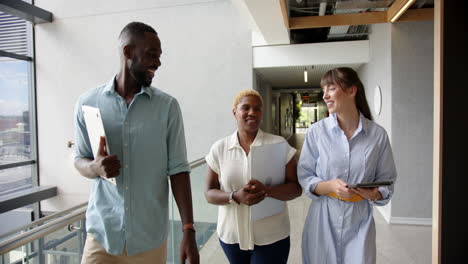 walking in office hallway, diverse colleagues holding tablets and documents, smiling