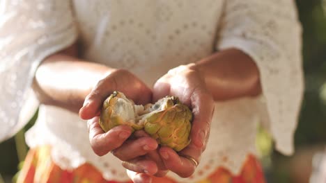 Woman-in-white-shirt-and-plaid-skirt-opening-sweetsop,-showing-to-camera