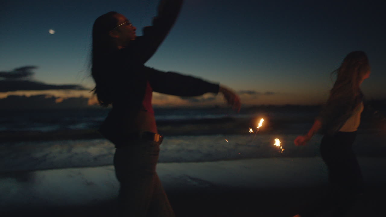 mejores amigos bailando con bengalas en la playa por la noche chicas adolescentes celebrando la víspera de año nuevo divirtiéndose bailando con fuegos artificiales de bengala junto al mar