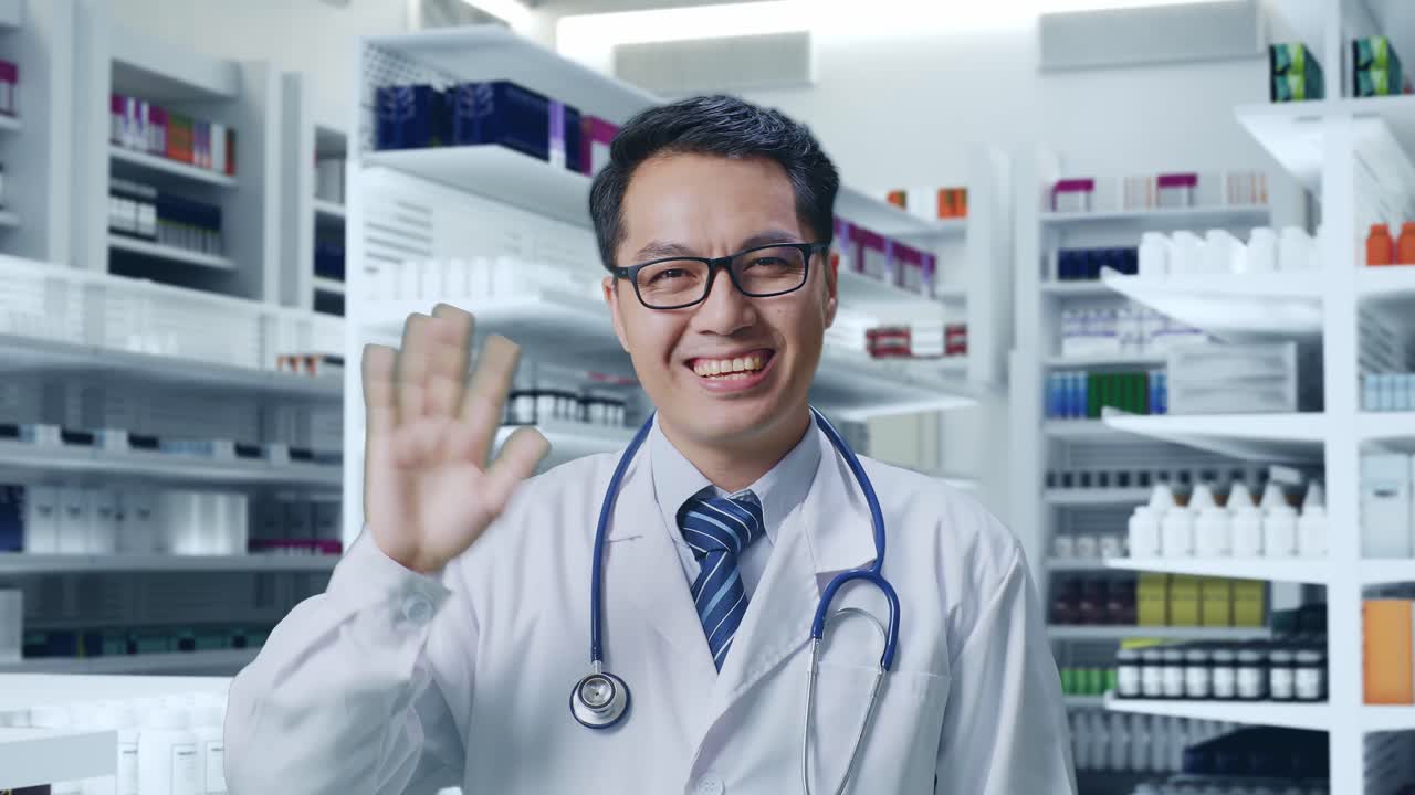 스테토스코프를 들고 있는 아시아 남성 의사가 약국에서 카메라에 손을 흔들고 미소 짓고 있습니다.
