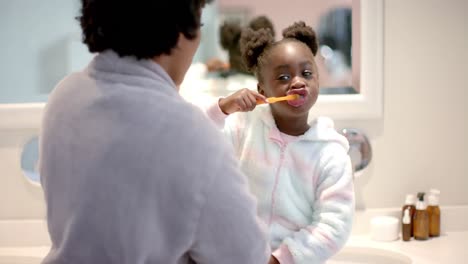 happy african american mother and daughter brushing teeth in bathroom, slow motion