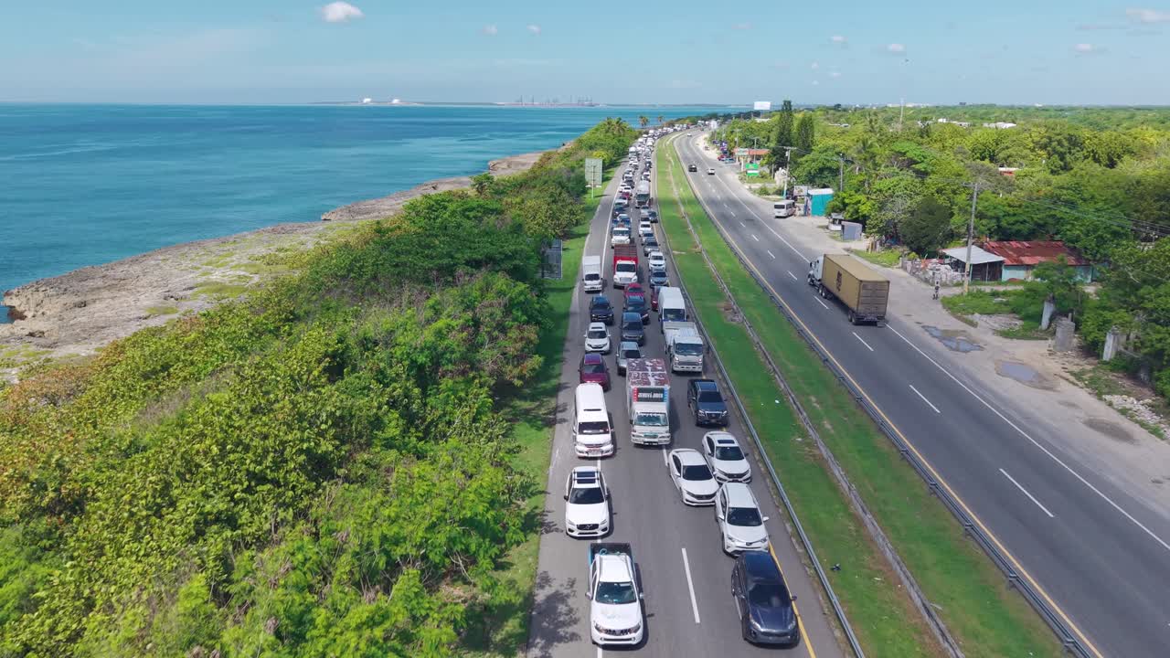 Major traffic jam on Las Américas Highway, long line of stationary cars next to beautiful Caribbean coast, Dominican Republic. Aerial forward