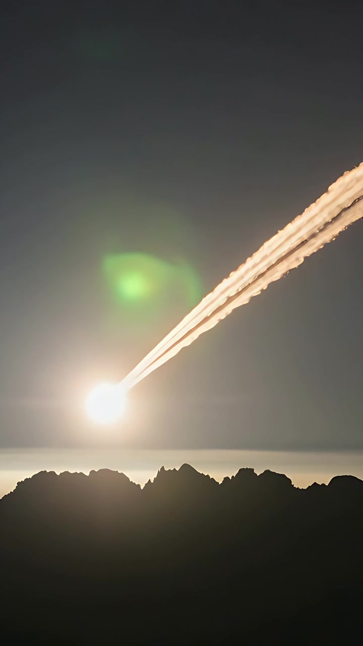 Vertical video: Brightening source sending streaking plume over mountain ridge, shedding sparks