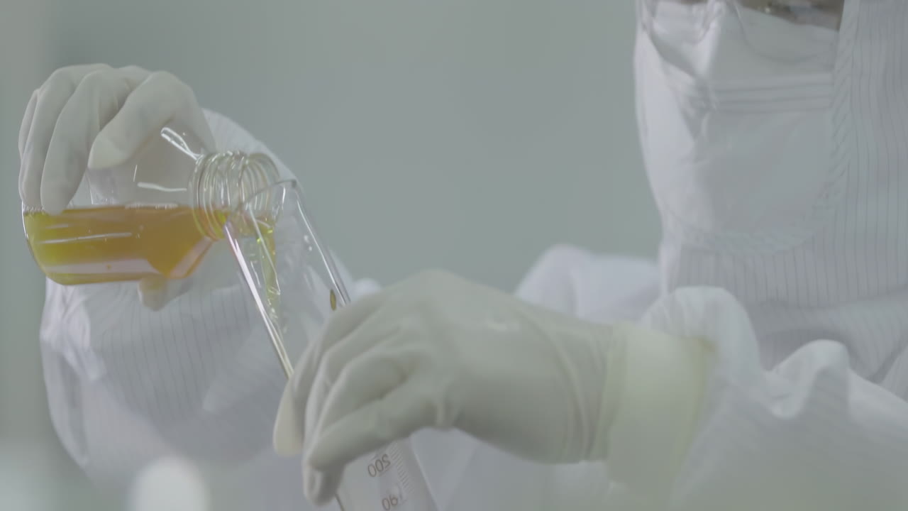 Medical worker in lab coats wearing safety goggles conducting biological experiment with dispensing chemical liquid into tissue culture flask for cell culture assay in biological cabinet facility