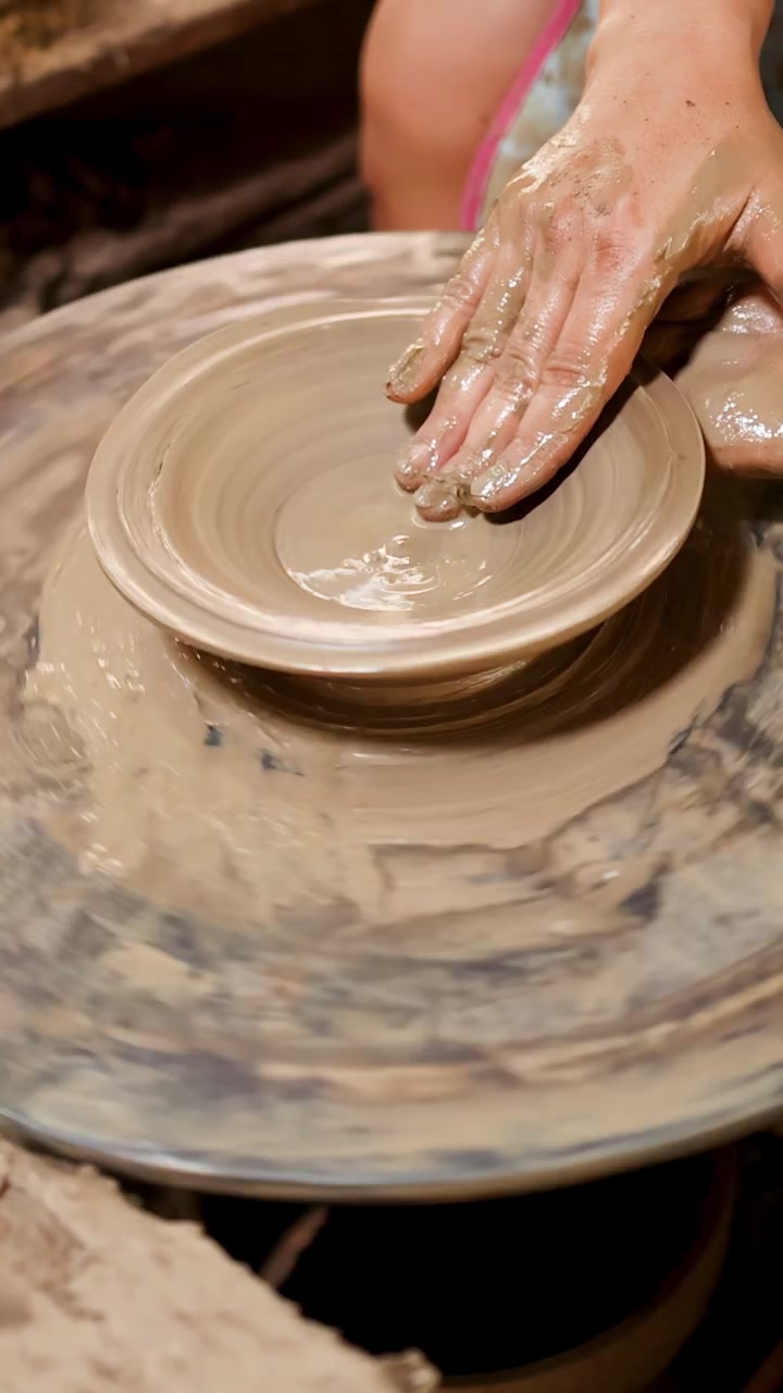 Primo piano di mani esperte che modellano argilla umida in una ciotola su un tornio.