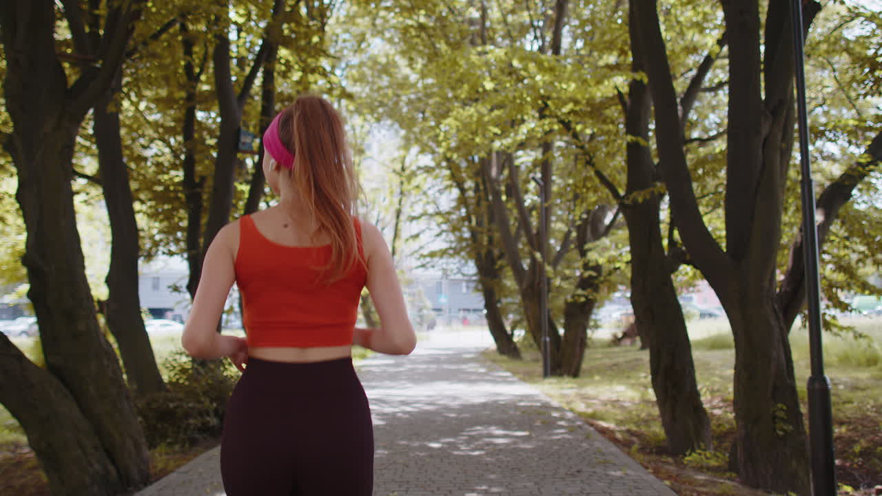 vista de atrás de un corredor de deporte atlético niña adulta entrenando maratón, escuchando música en auriculares