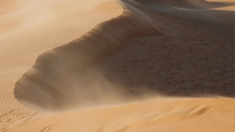 wind blowing sand across a golden desert dune