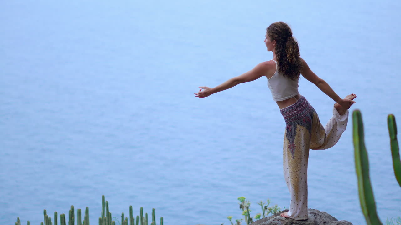en el encantador resplandor de la puesta de sol y el océano azul, una joven practica yoga en una orilla rocosa, encarnando un estilo de vida saludable, armonía y la interacción entre los seres humanos y la naturaleza