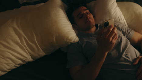 depressed man laying on bed and picking up phone, soft light