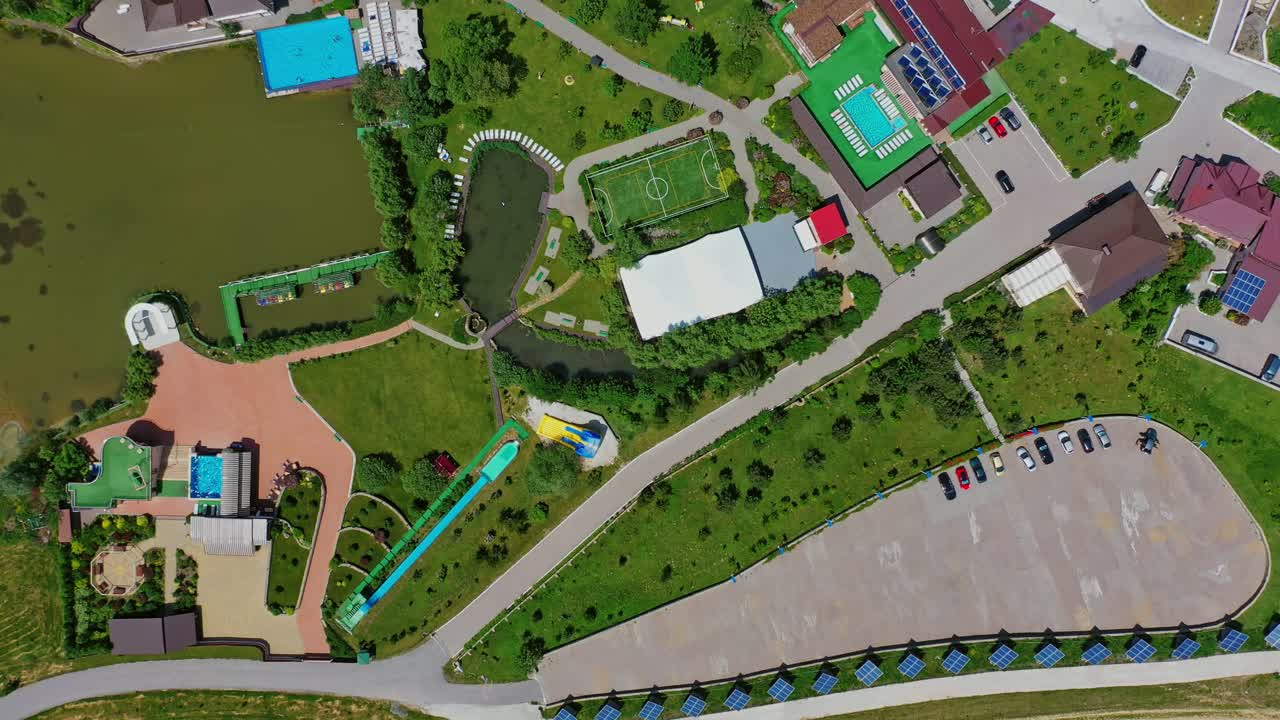 Panoramic view of a modern complex. Recreation area with football pitch and swimming pool near the river. Resting center among green nature. Top aerial view.