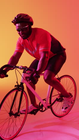 vertical video of happy african american male cyclist riding on orange background