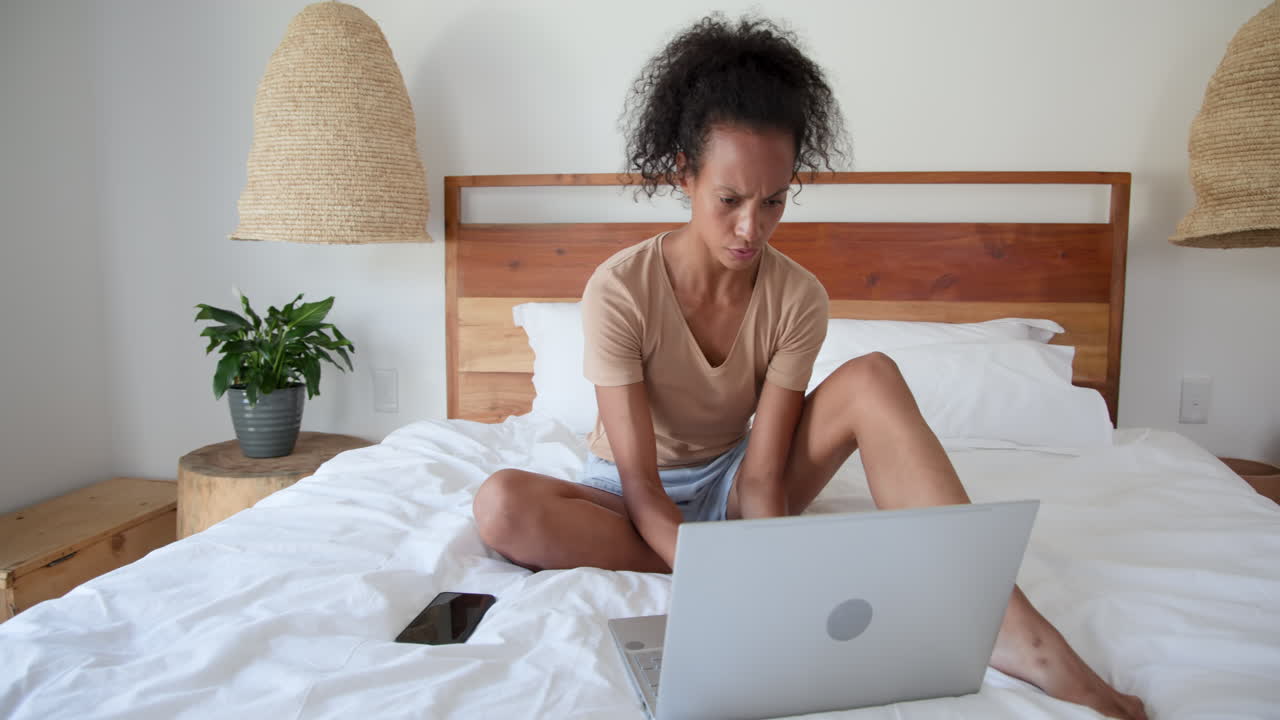 woman sitting on bed using laptop and smartphone at home