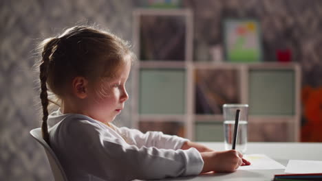 unhappy girl draws picture sitting at table in kindergarten