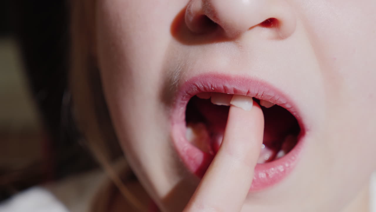 소녀는 곧 빠질 젖니로 손가락을 흔들고 있다