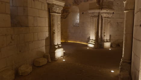 ancient stone crypt with romanesque columns and medieval frescoes, dimly lit interior