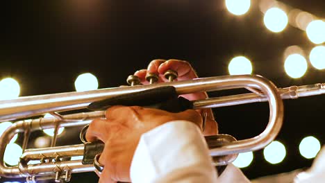 close up of adult male playing the trumpet at a show at night, with bright lights in background