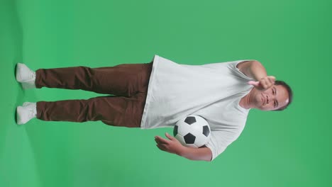 full body of asian man with a ball showing thumbs down gesture for making fun of the losers while cheering soccer on green screen background