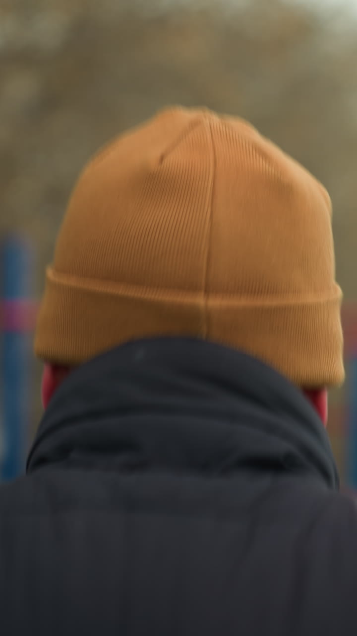 vista trasera de un entrenador con una gorra marrón corriendo rápido en un gimnasio al aire libre, con una vista borrosa de un coche pasando y barras de hierro rojas y azules en el fondo