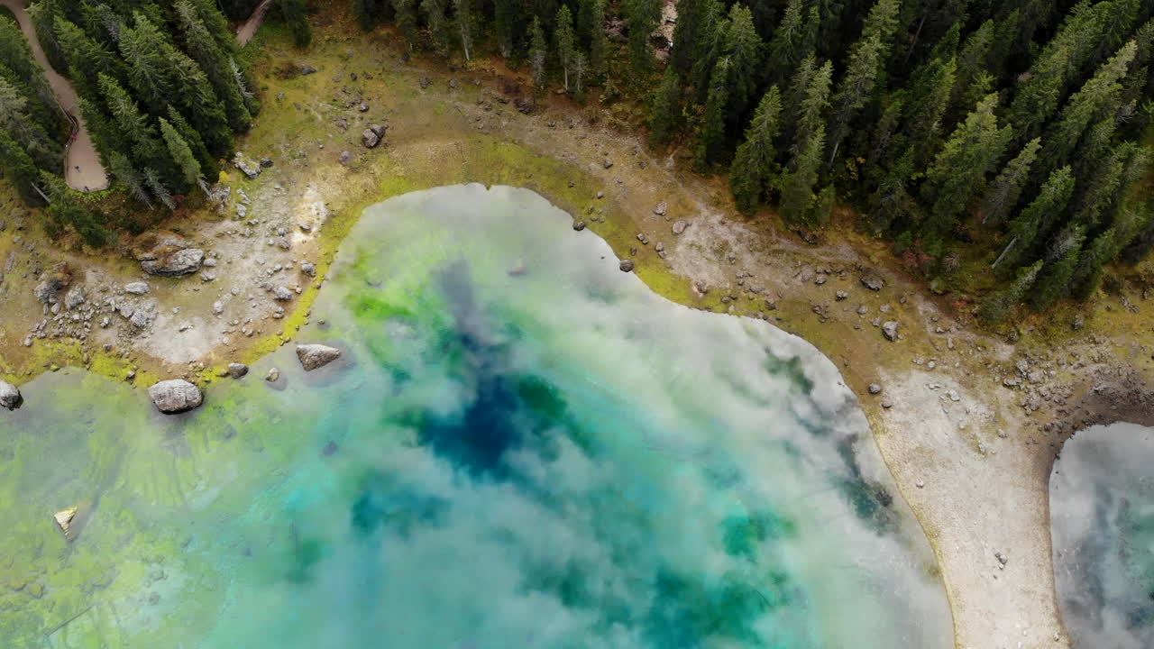 drone flying over beautiful reflective glacier lake surrounded by trees in Dolomites in Italy
