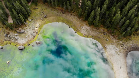 drone volando sobre un hermoso lago glaciar reflectante rodeado de árboles en dolomitas en italia