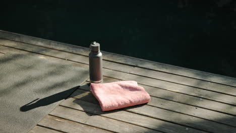 yoga mat, water bottle, and towel on wooden deck by pool, copy space