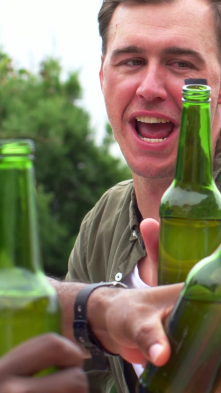 Video verticale: Tifoso in maglietta verde con pittura a tema tedesco che saluta e alza bottiglie di birra verde in giardino.