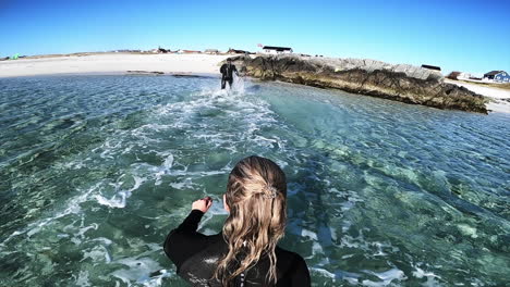 third person view of a couple in wetsuits splashing through cold water in the nordic ocean