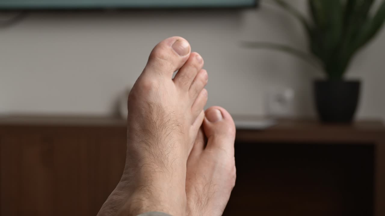 Concetto di pigrone da divano: uomo a piedi nudi sdraiato sul divano che guarda la TV, primo piano dei piedi