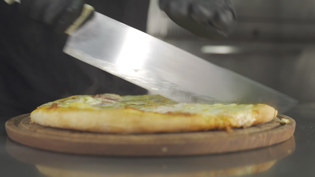 Close up view of chef cutting freshly made pizza into slices with kitchen knife