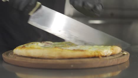 close up view of chef cutting freshly made pizza into slices with kitchen knife