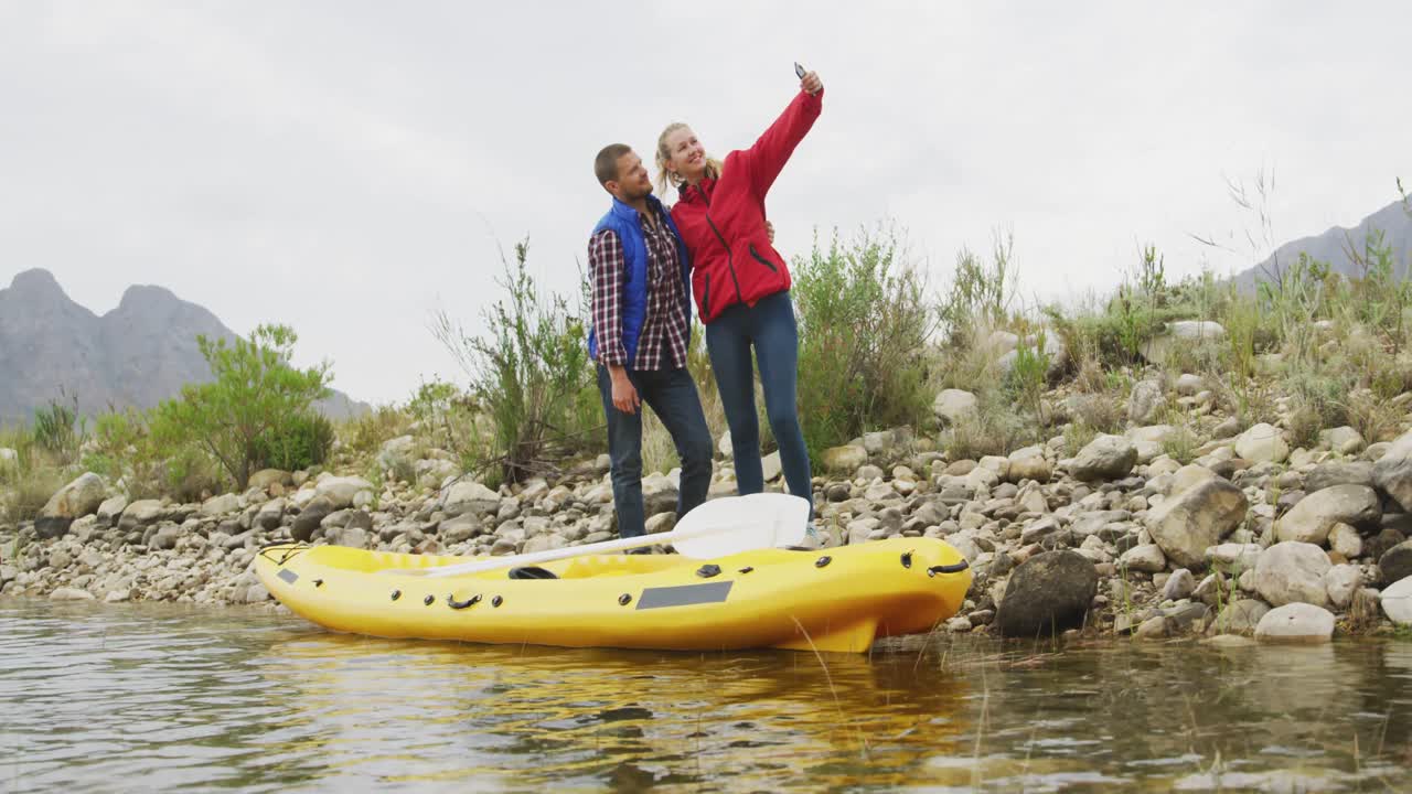 pareja caucásica pasando un buen rato en un viaje a las montañas, de pie al lado de un kayak, tomando un s