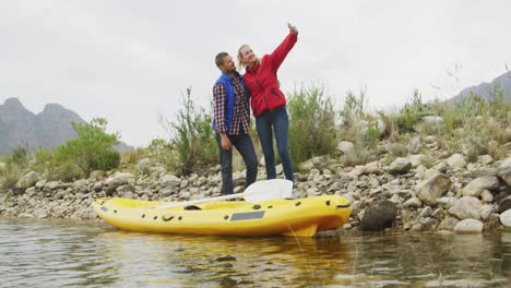 caucasian couple having a good time on a trip to the mountains, standing next to a kayak, taking a s