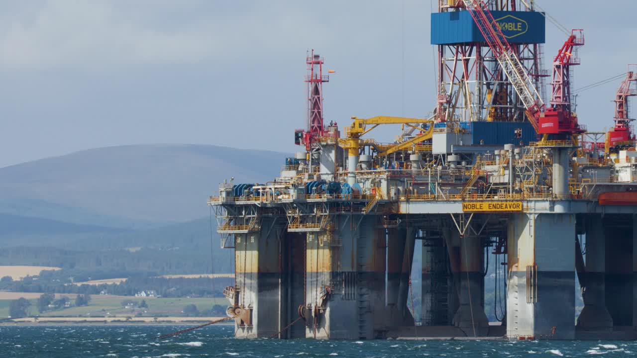 Stor offshore-olieplatform nær den skotske kyst, stationær på roligt vand med fjerne bakker