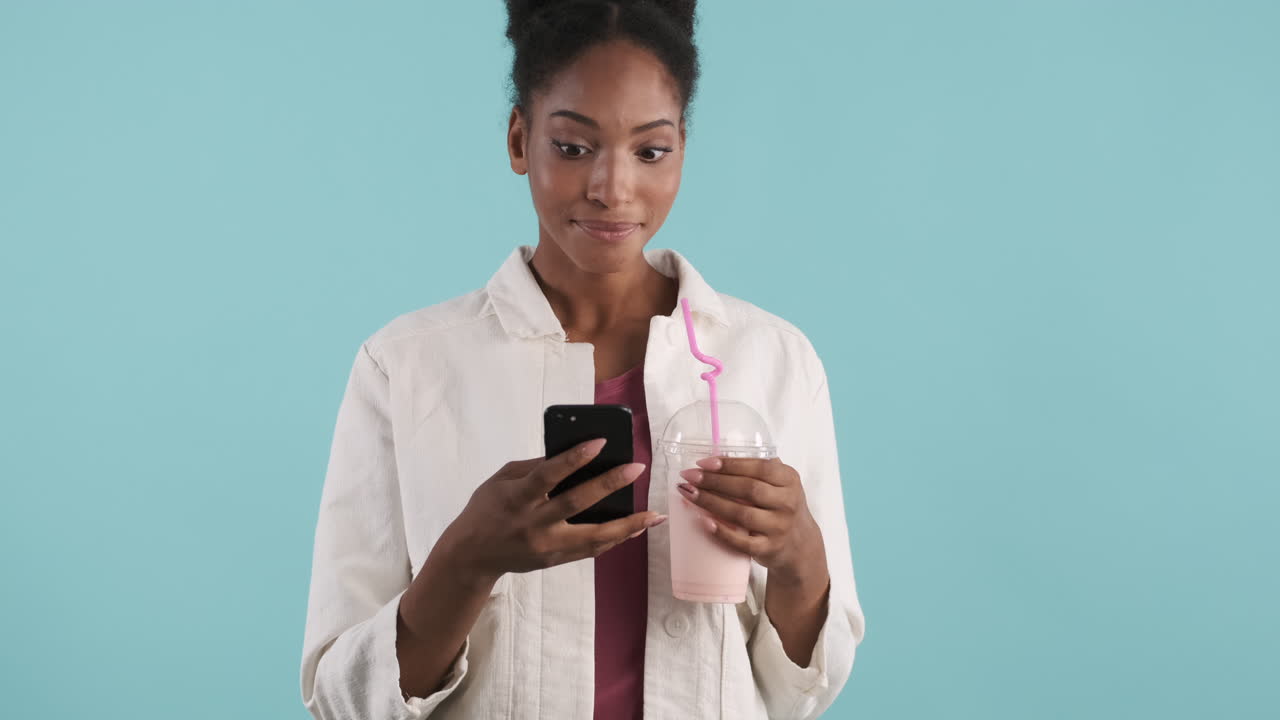 Smiling woman drinking milkshake and using phone