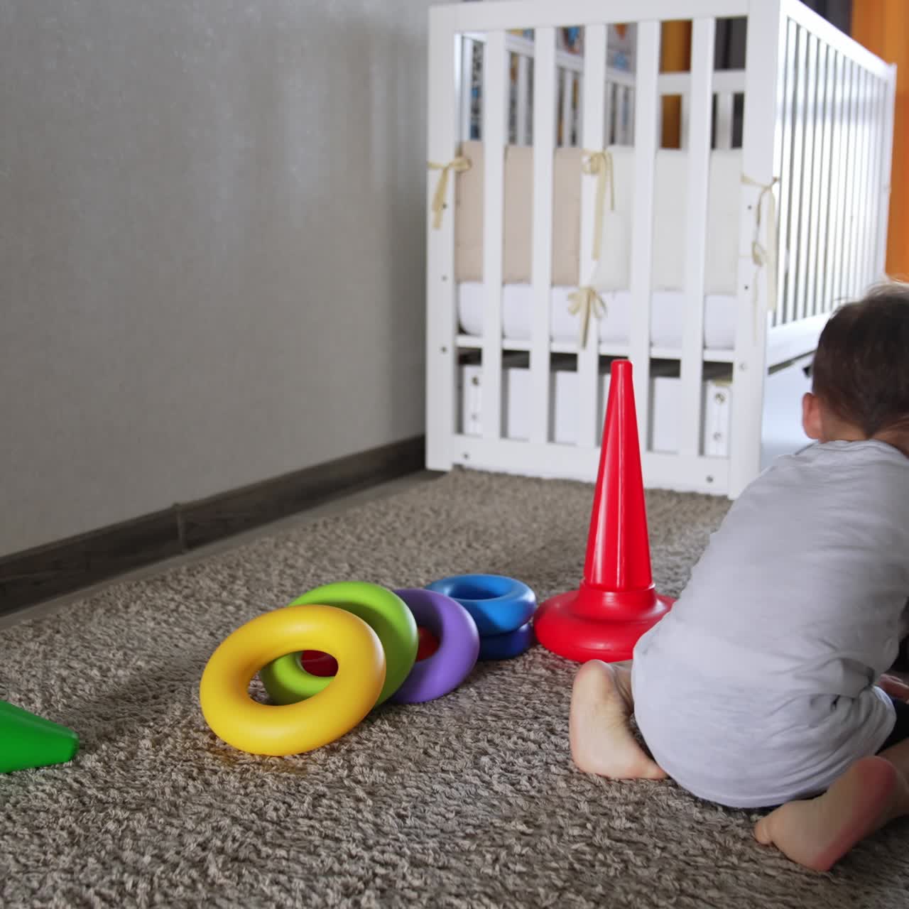Cute black cat lies in the kid's room near the toy pyramid. Baby boy comes up to the animal to pet it